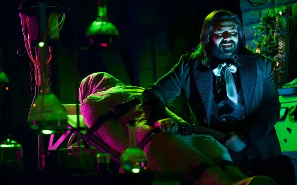 A vibrant HD wallpaper from What We Do in the Shadows, featuring Matt Berry in a dimly lit lab, animatedly interacting with a figure wrapped in a shroud, enhanced by colorful lighting effects.