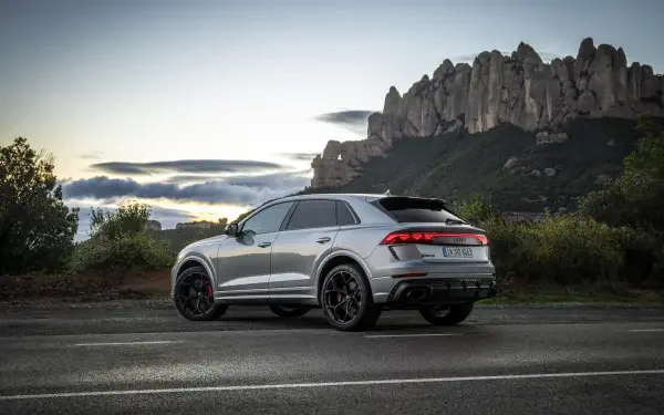 A stunning 4K Ultra HD wallpaper featuring a sleek Audi RS Q8 parked on a scenic road, with dramatic mountains in the background under a colorful sky at dusk.
