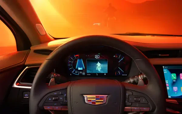 The image showcases the interior of a Cadillac XT6, featuring a vibrant orange backdrop and a view of the dashboard with advanced controls and display screens.