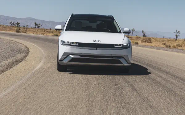 A sleek Hyundai IONIQ 5 drives along a curved road, framed by a desert landscape. This 4K Ultra HD image captures the car's modern design and dynamic stance.