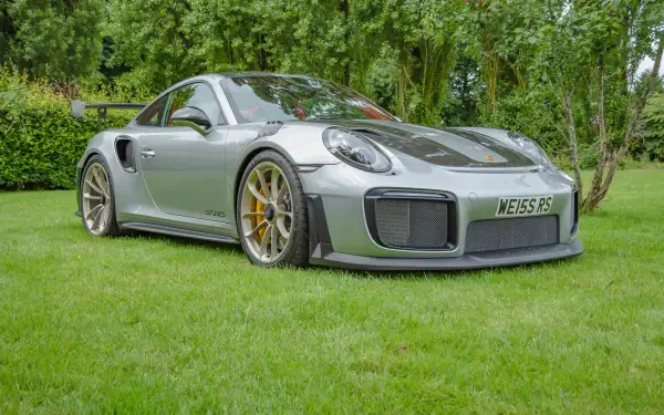 Silver Porsche sports car on a green lawn with trees, high-detail 5K Ultra HD PC desktop wallpaper and background highlighting sleek bodywork and gold brake calipers.