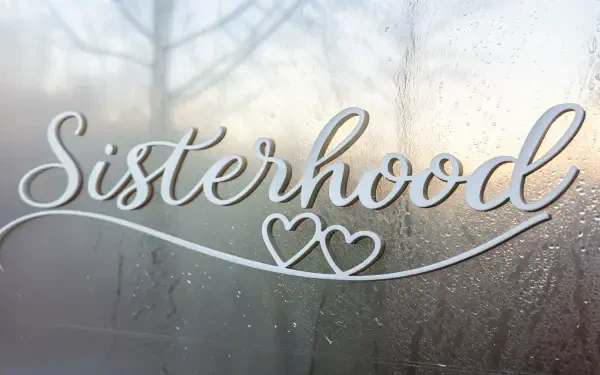 A close-up of the word Sisterhood elegantly scripted on a misty surface, with soft lighting in the background, creating a warm and inviting 4K Ultra HD wallpaper.