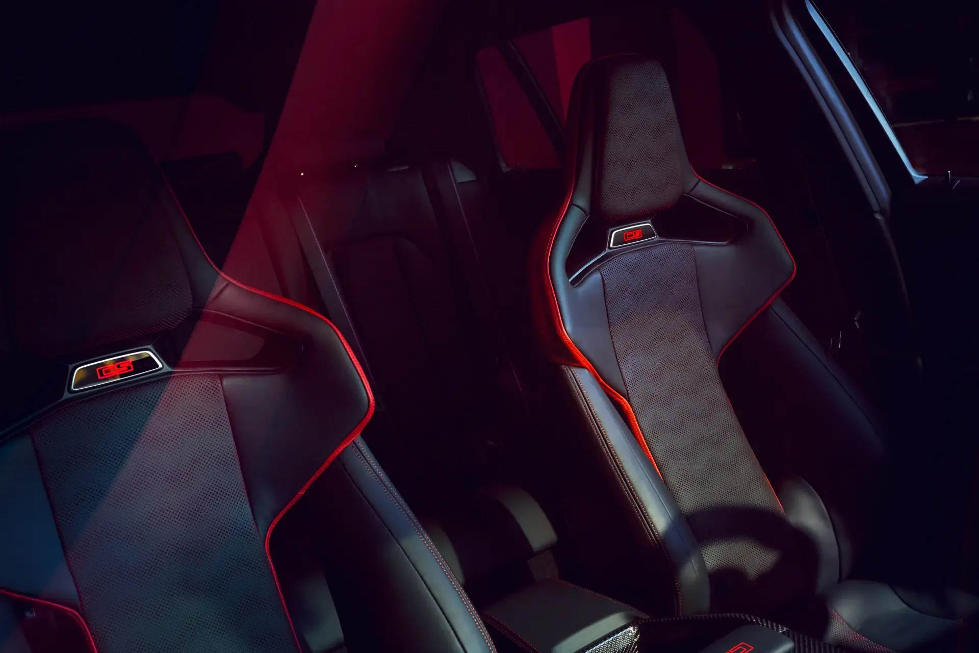 Close-up of the BMW M3 CS Touring's sleek interior, featuring stylish sports seats with striking red accents, set against a dramatic lighting backdrop. High-definition wallpaper.