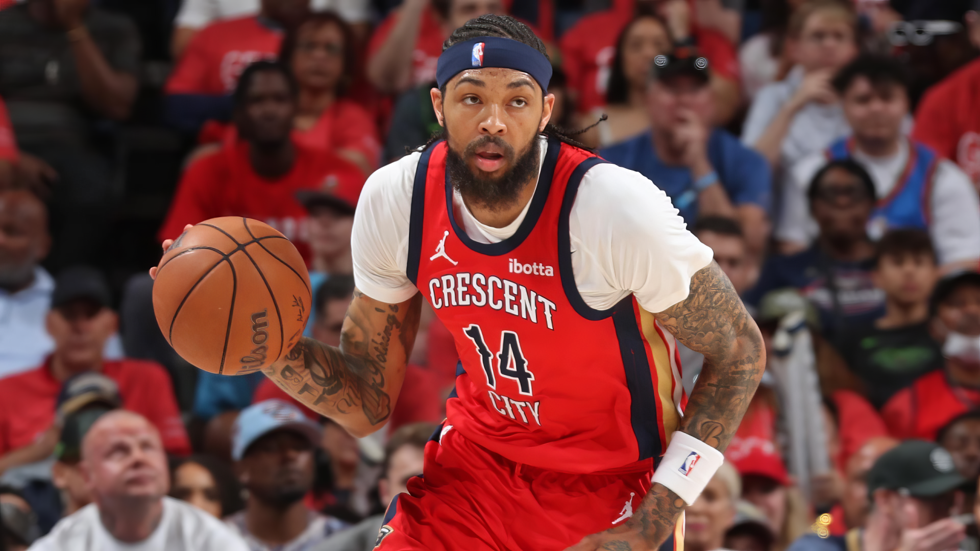 Brandon Ingram dribbles the basketball while wearing the New Orleans Pelicans' red jersey, showcasing his skills on the court amidst a cheering crowd. HD wallpaper for basketball fans.