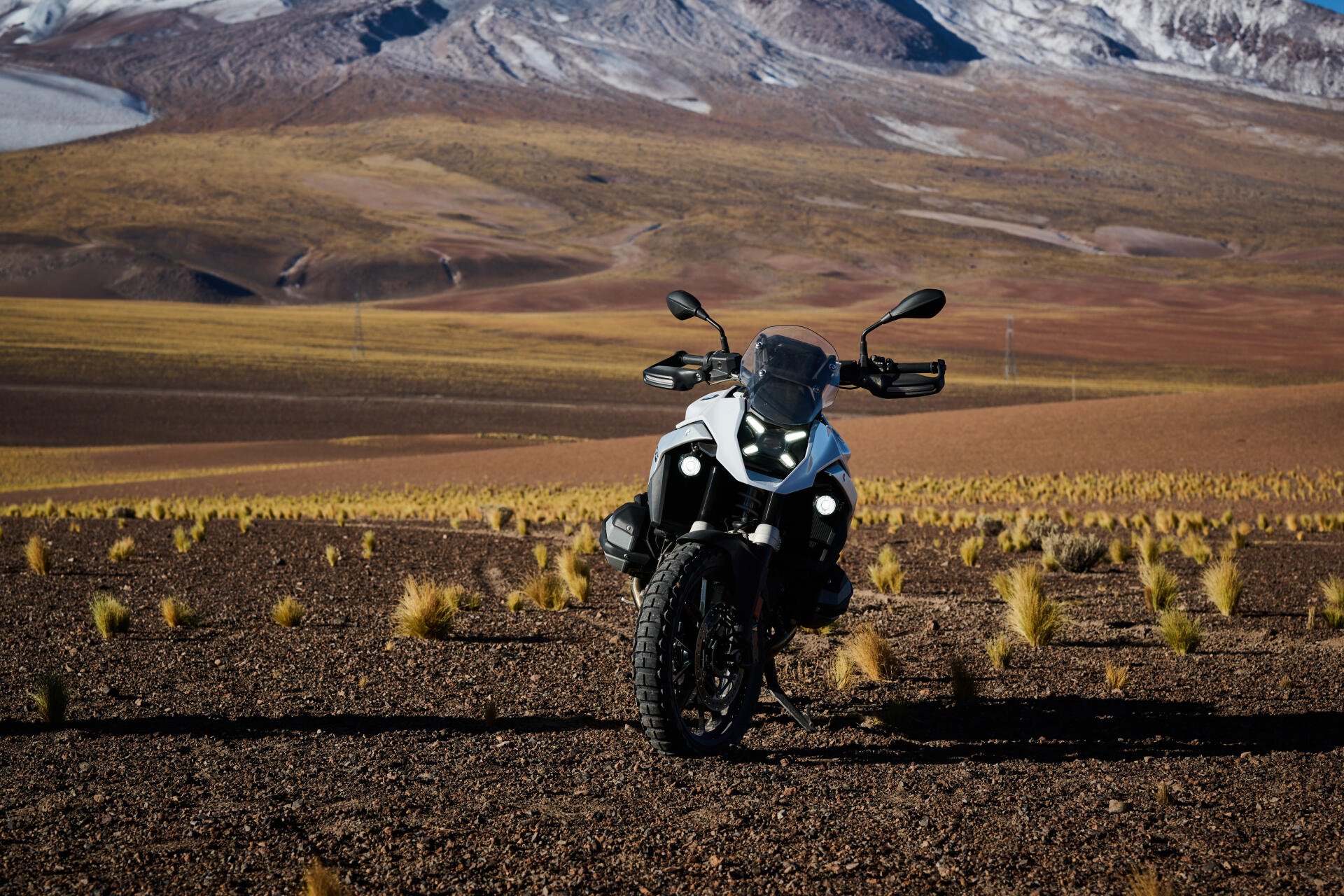 A striking BMW R1300GS motorcycle stands on rugged terrain, set against a backdrop of mountains and golden grasses, captured in vibrant 4K Ultra HD.