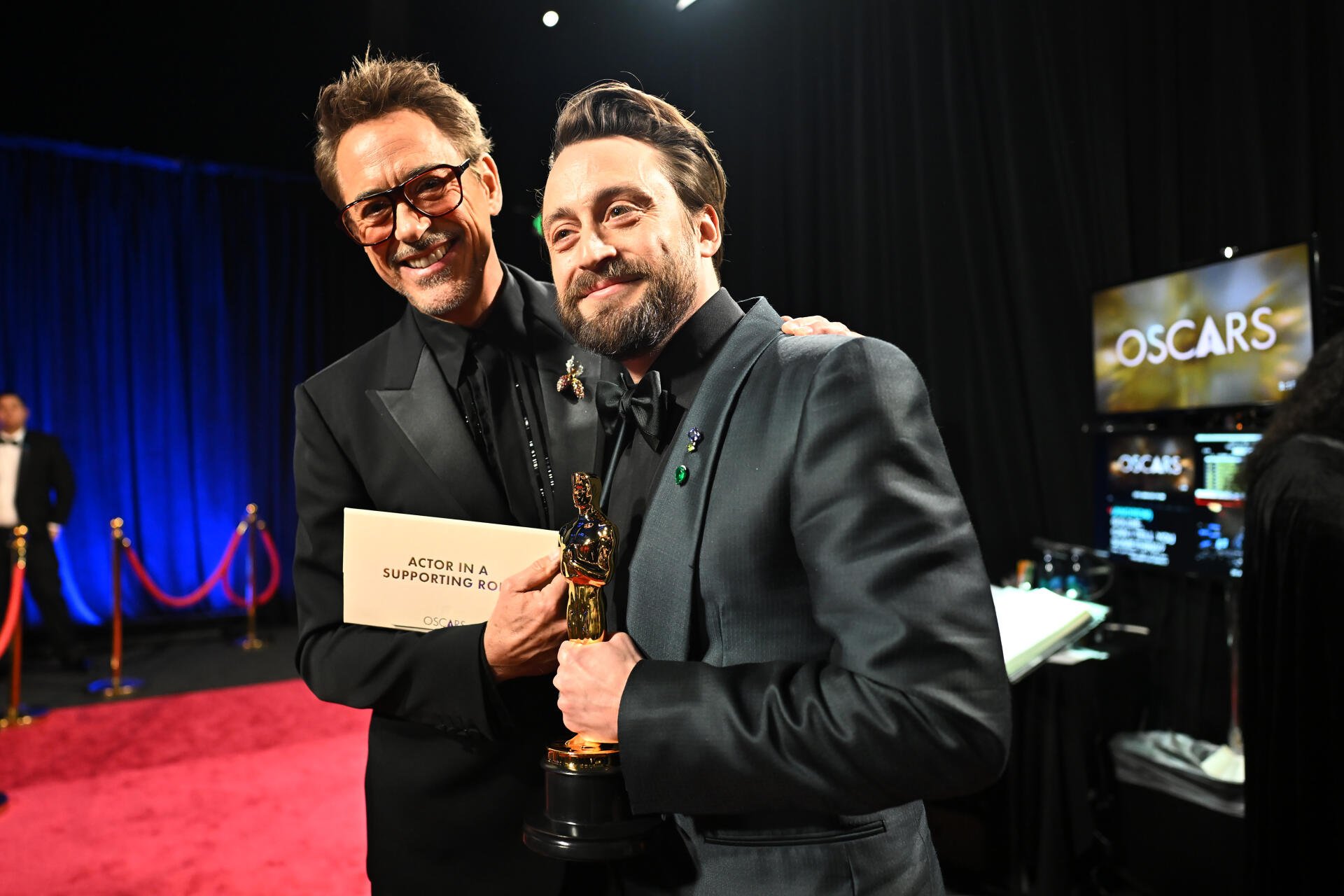 Robert Downey Jr. and Kieran Culkin embrace on the red carpet at the Academy Awards, celebrating remarkable achievements in film. The backdrop features the Oscars logo, enhancing the moment's significance.