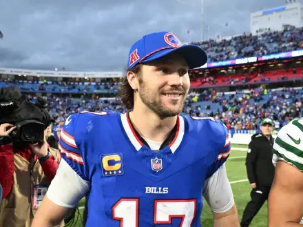 Josh Allen smiles on the field after a game, wearing a Buffalo Bills jersey and cap. The image captures the excitement of NFL football, showcasing the team's spirit and camaraderie.