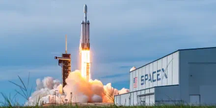 A dramatic HD desktop wallpaper featuring a SpaceX rocket launching against a cloudy sky, with smoke billowing from the launch pad and the SpaceX building in view.