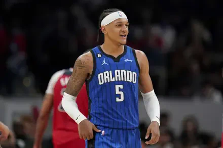 Orlando Magic player Paolo Banchero smiles on the court, wearing the team's blue jersey and headband, featured as a vibrant HD desktop wallpaper.