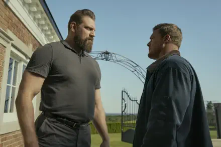HD desktop wallpaper featuring Alan Ritchson and Olivier Richters from the TV show Reacher, standing face-to-face outdoors near a gated entrance.