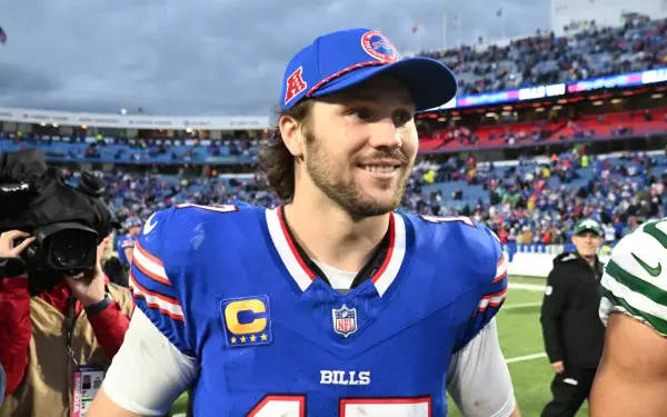 Josh Allen smiles on the field after a game, wearing a Buffalo Bills jersey and cap. The image captures the excitement of NFL football, showcasing the team's spirit and camaraderie.