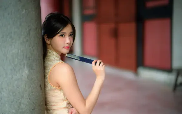 8K Ultra HD PC desktop wallpaper: young woman in a cheongsam leaning against a pillar, holding a book near her shoulder, soft-focus corridor background.