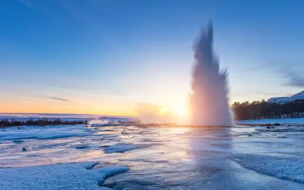 A stunning view of Strokkur Geyser in Iceland, surrounded by snow, erupts against a vibrant sunset sky. This 4K Ultra HD image captures the beauty of nature.