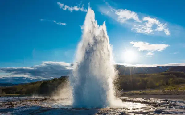 A stunning 4K Ultra HD image of Strokkur Geyser in Iceland, showcasing a powerful water eruption against a bright blue sky and sunlit landscape.