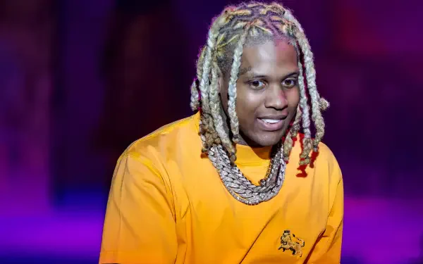 A vibrant HD wallpaper featuring rapper Lil Durk, captured with a playful smile, wearing an eye-catching orange outfit and notable jewelry against a colorful background.