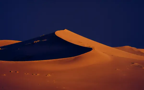 A stunning 4K Ultra HD image of Sahara sand dunes, showcasing the contrasting colors of golden sands against a deep blue sky, creating a serene desert landscape.