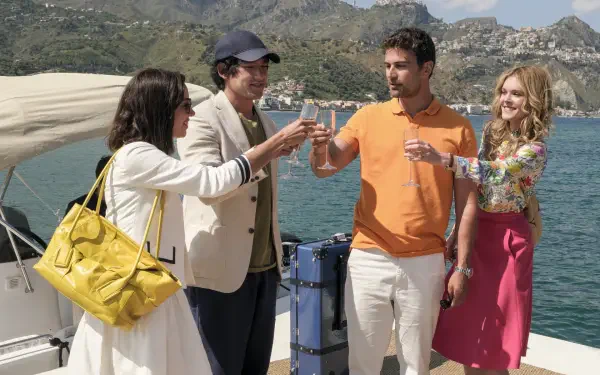 HD desktop wallpaper featuring cast members of the TV show The White Lotus toasting on a boat against a scenic coastal mountain backdrop.