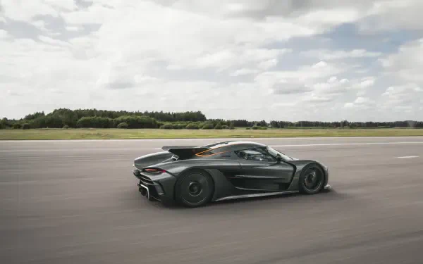 A sleek Koenigsegg Jesko Absolut accelerates on an open road under a partly cloudy sky, captured in stunning 8K Ultra HD quality for an immersive desktop wallpaper experience.
