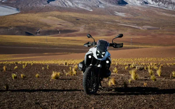 A striking BMW R1300GS motorcycle stands on rugged terrain, set against a backdrop of mountains and golden grasses, captured in vibrant 4K Ultra HD.