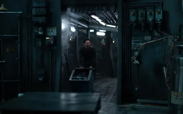 A scene from the 2025 movie Mickey 17, featuring Steven Yeun in a dimly lit, industrial setting, surrounded by machinery and electrical panels, creating a tense atmosphere.