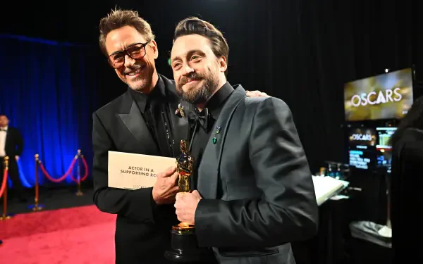 Robert Downey Jr. and Kieran Culkin embrace on the red carpet at the Academy Awards, celebrating remarkable achievements in film. The backdrop features the Oscars logo, enhancing the moment's significance.