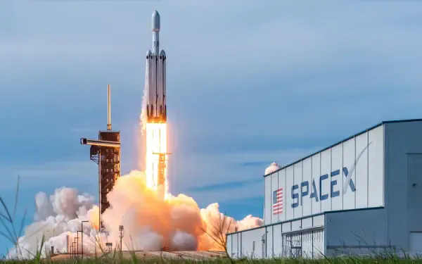 A dramatic HD desktop wallpaper featuring a SpaceX rocket launching against a cloudy sky, with smoke billowing from the launch pad and the SpaceX building in view.