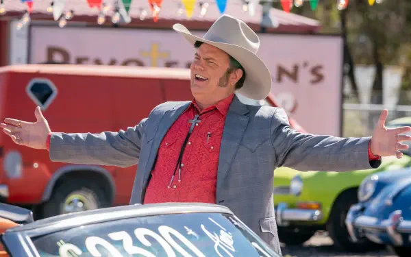 A vibrant HD wallpaper from the TV show Dark Winds, featuring Rainn Wilson in a cowboy hat, enthusiastically presenting a classic car against a colorful backdrop.