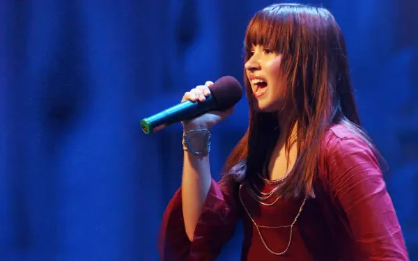 HD desktop wallpaper showing a Camp Rock singer mid-song, holding a microphone onstage with blue curtains behind her.