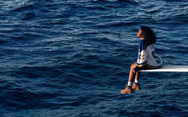 Album-cover style music wallpaper: a singer seated on a diving board over a vast blue ocean, HD PC desktop wallpaper and background.