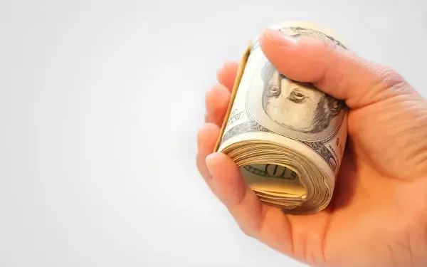 Close-up of a hand gripping a rolled stack of US dollar banknotes on a white background — HD PC desktop wallpaper.