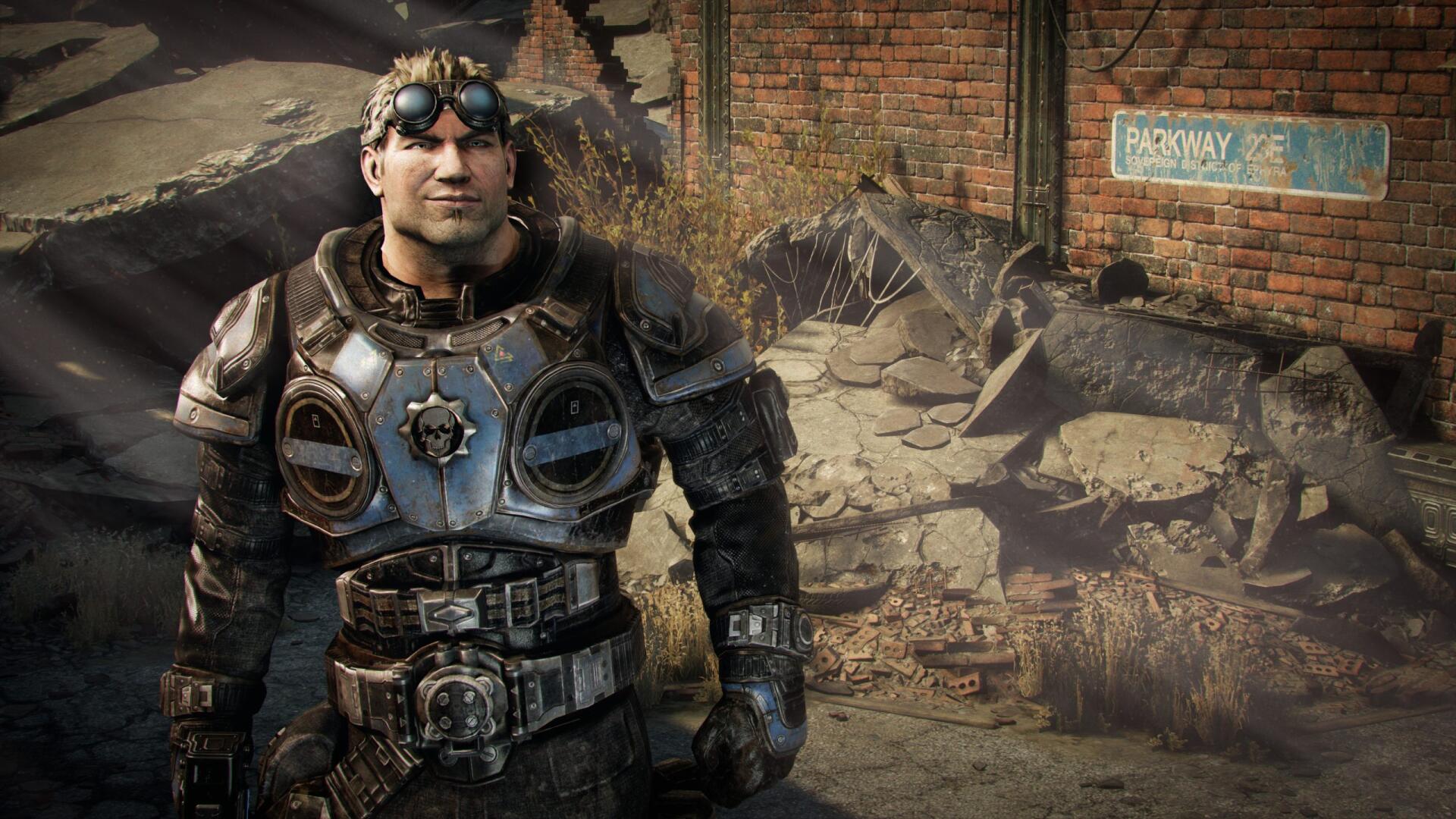 HD PC desktop wallpaper, video game Gears Of War: Reloaded — an armored soldier in heavy combat gear stands amid rubble by a cracked brick wall in a ruined urban street.