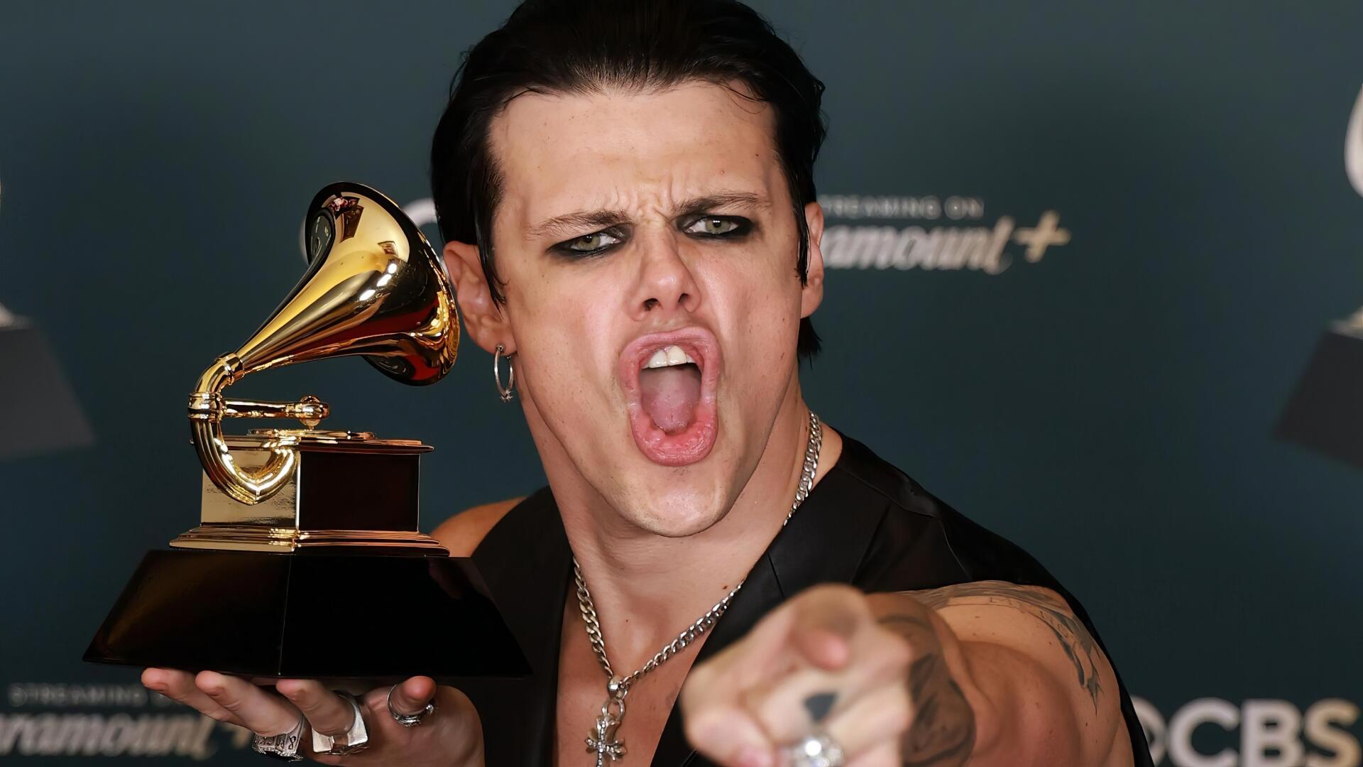 2K Quad HD desktop wallpaper of a punk-rock singer at the Grammy Awards, heavy eye makeup, clutching a Grammy trophy and pointing aggressively toward the camera, music energy and stage presence.