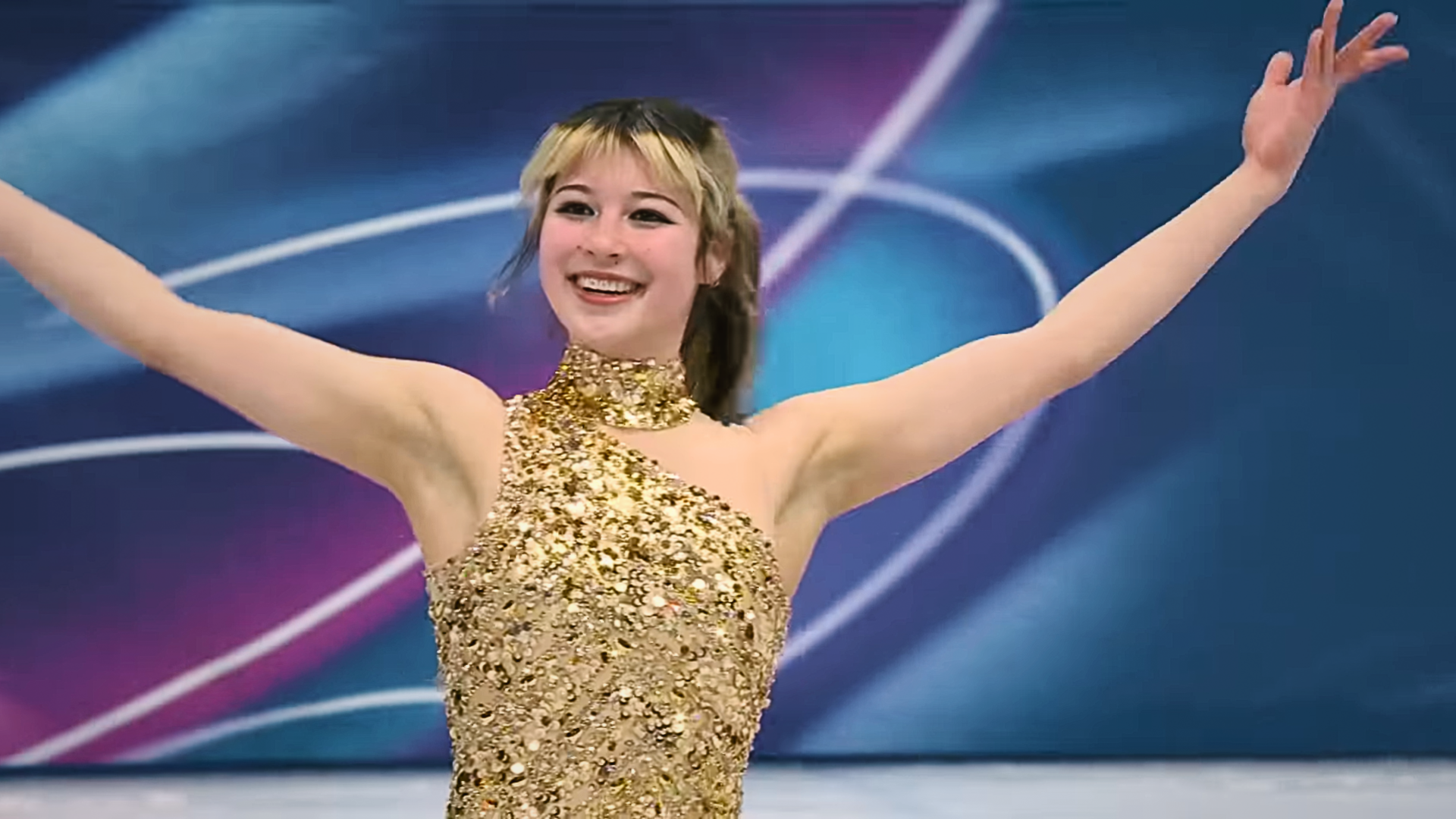 Smiling female figure skater in a gold sequined costume, arms raised on a Winter Olympics–style ice rink, 4K Ultra HD desktop wallpaper.