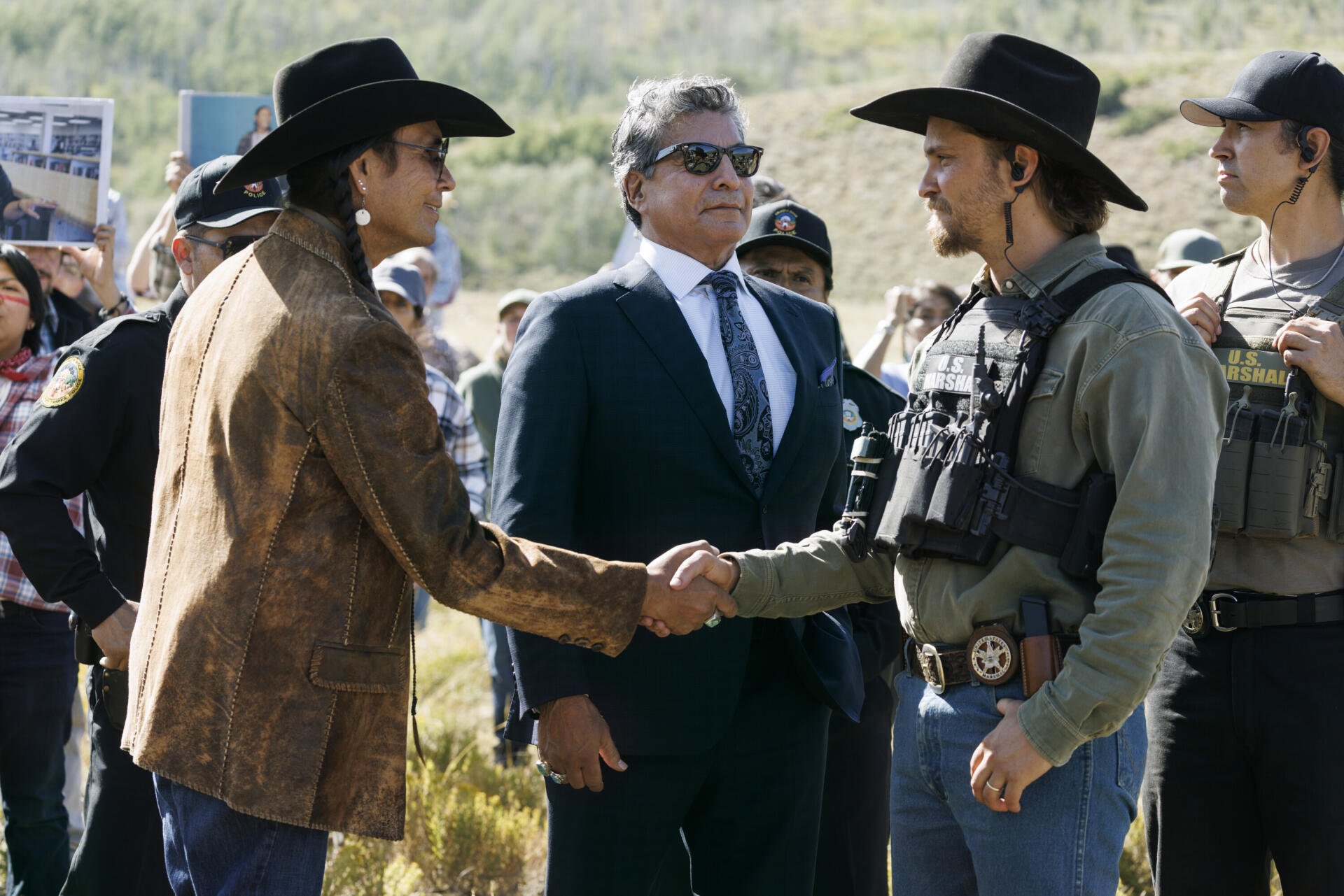 TV show marshals: two men in cowboy hats shake hands as tactical marshals and a suited official watch — 2K Quad HD PC desktop wallpaper/background.