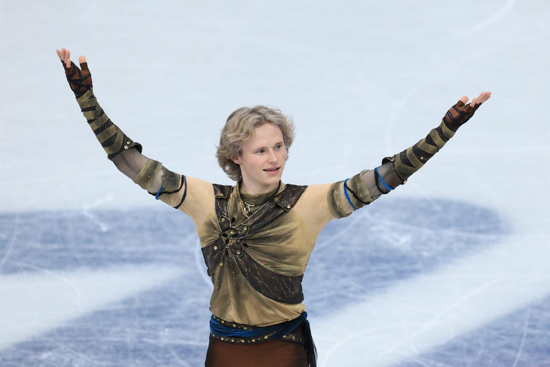 Ice skater at the Winter Olympics, arms raised in a gold-and-green costume on the icy rink — HD PC desktop wallpaper and background.