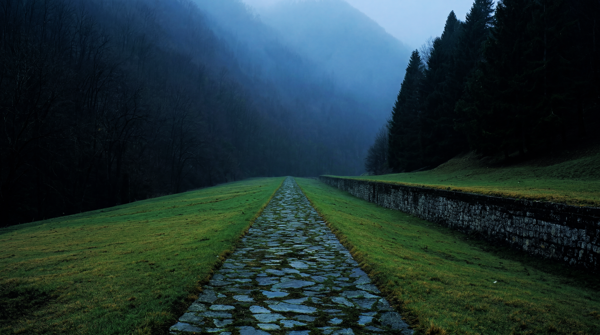 5K Ultra HD PC desktop wallpaper of a cobblestone mountain trail cutting through foggy, dark woods and stormy, mist-shrouded peaks.