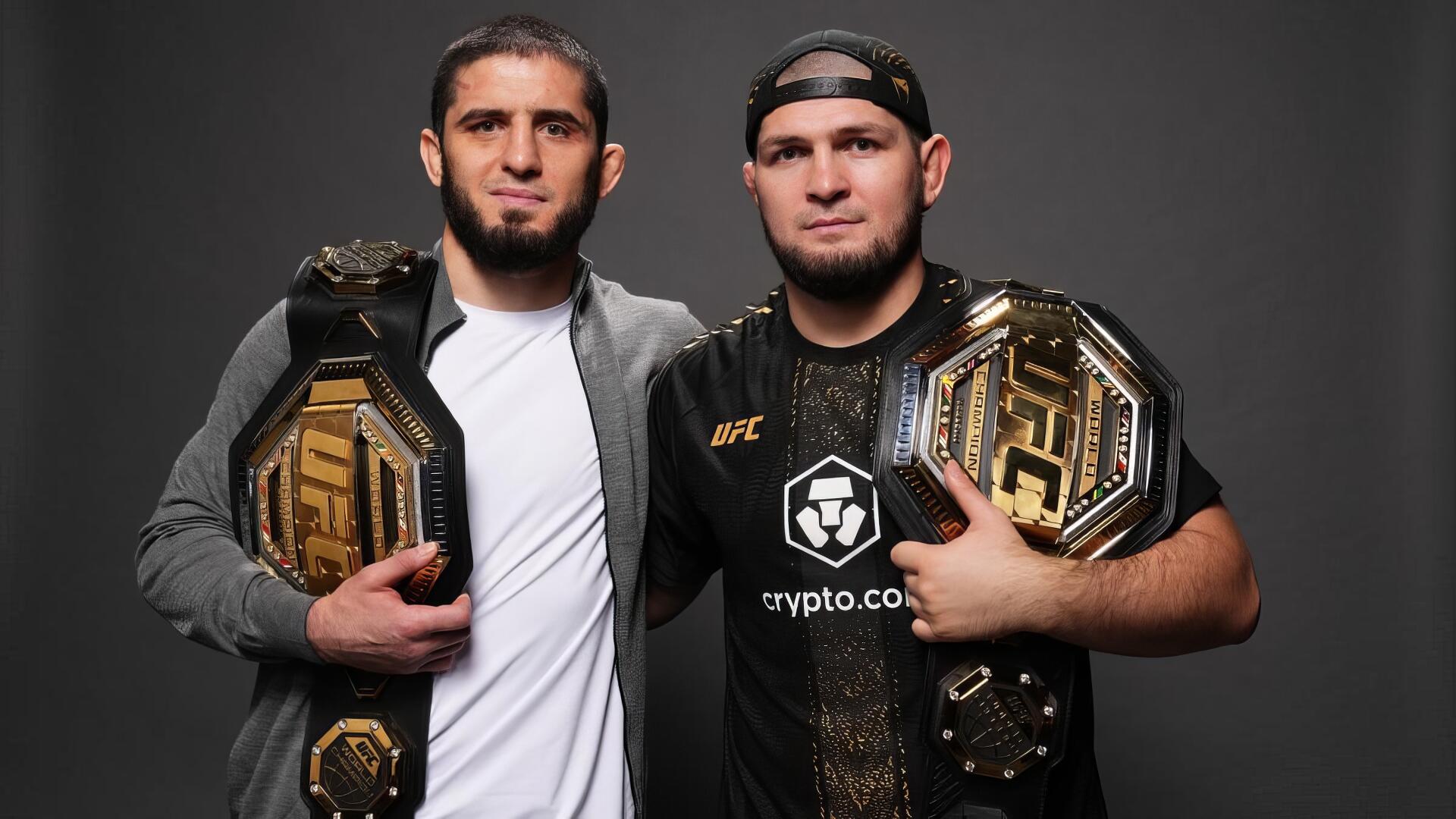 HD desktop wallpaper of two UFC champions posing shoulder-to-shoulder with gold title belts, one in a jacket and the other in a cap and black shirt, studio portrait on a gray background.