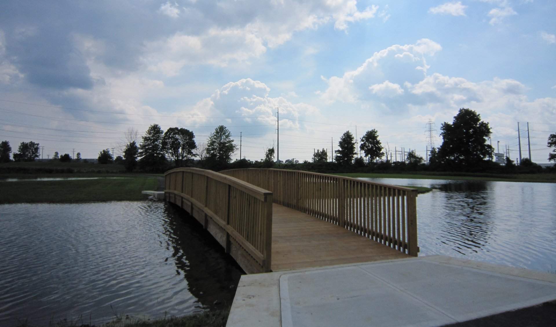 4K Ultra HD PC desktop wallpaper and background: man-made wooden footbridge arching over a calm pond with trees and a cloudy sky on the horizon.