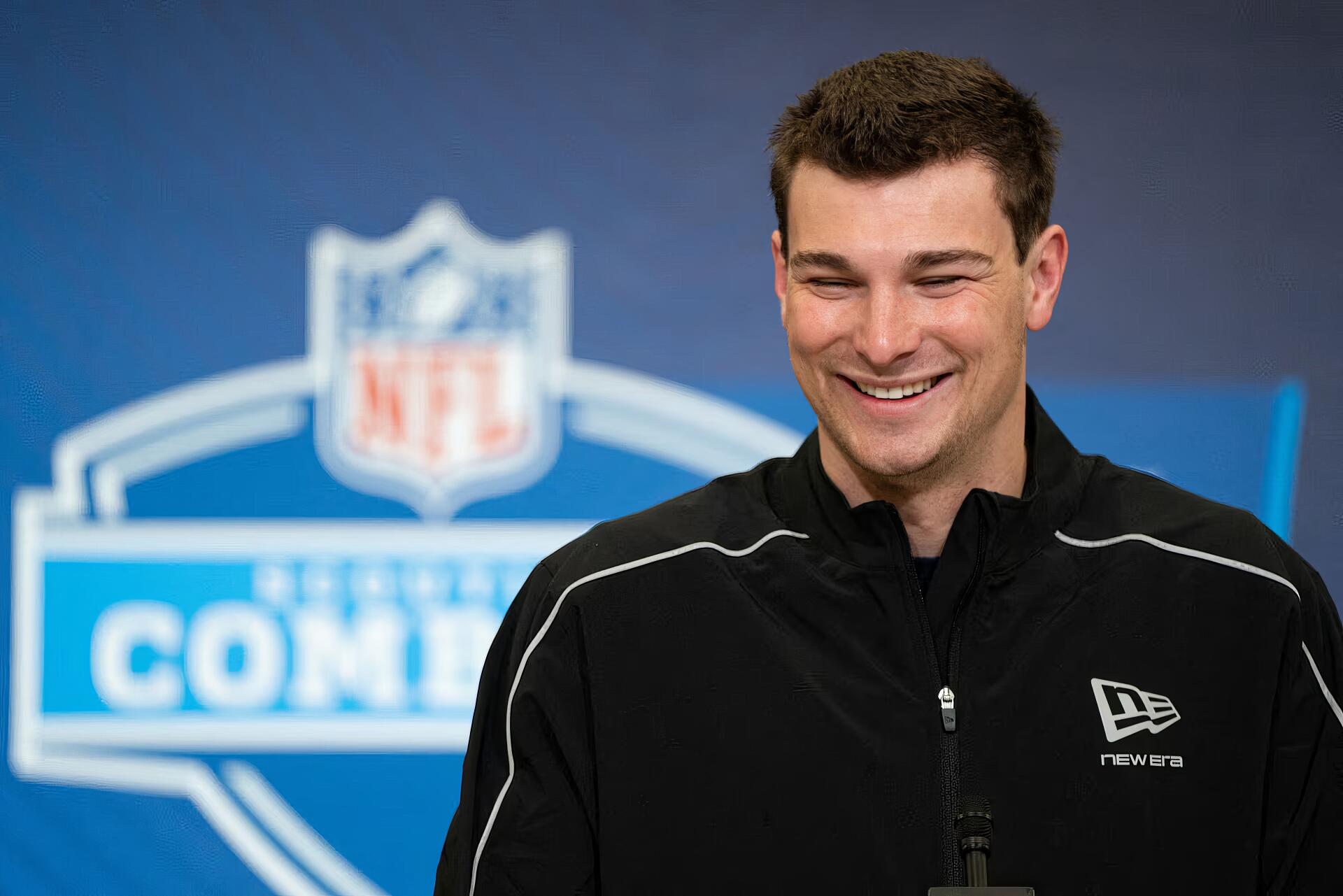 Smiling American man in front of an NFL logo press backdrop, 4K Ultra HD PC desktop wallpaper/background.