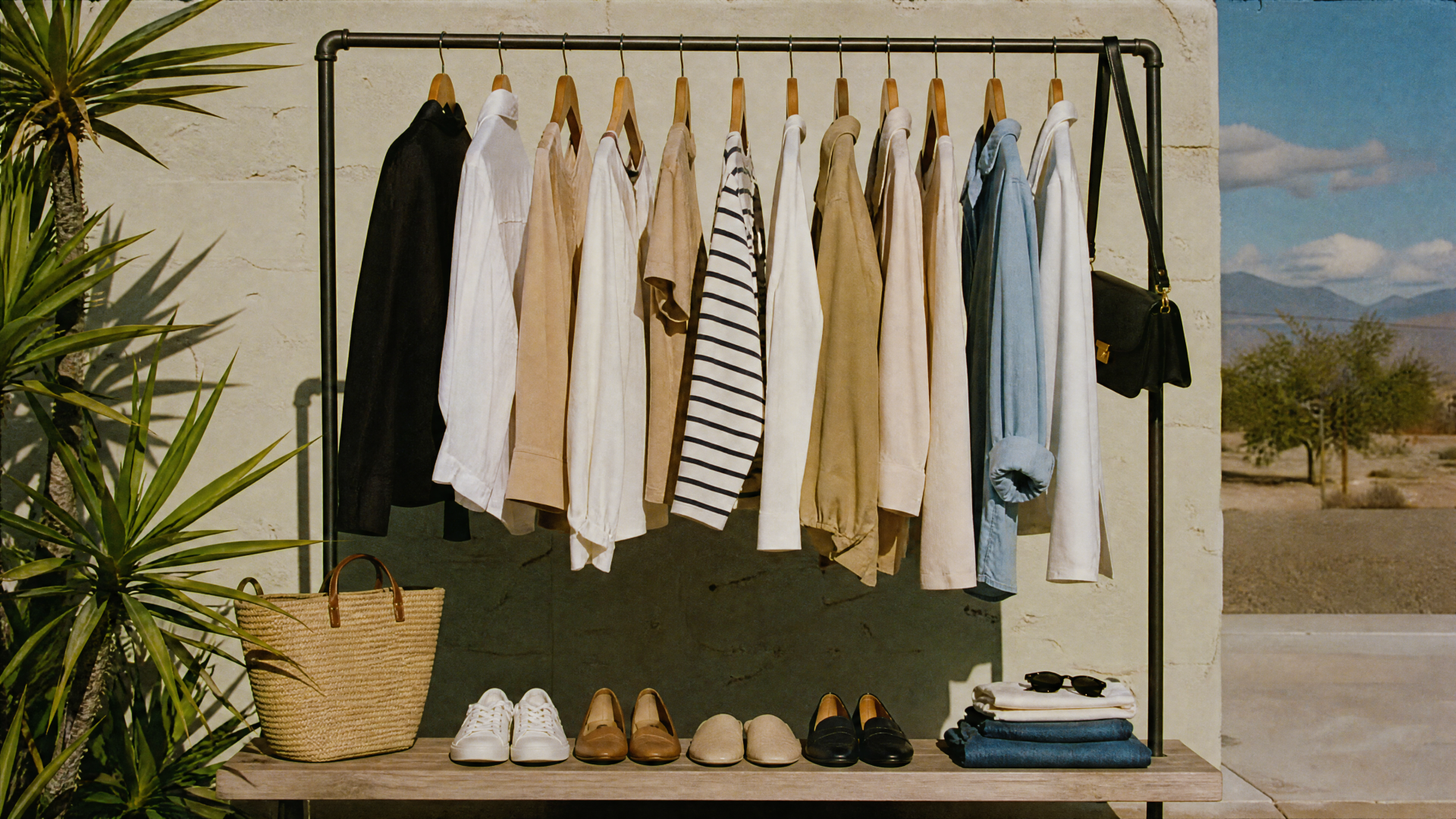 Capsule wardrobe: neutral shirts, jackets and a striped top on a rack with shoes, straw bag and sunglasses against a sunlit desert — 4K Ultra HD PC Desktop Wallpaper and Background.
