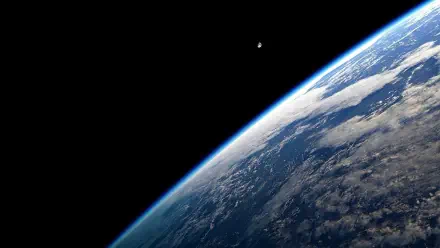 HD PC desktop wallpaper: space view of a planet from orbit—curved, cloud-covered surface with a bright limb and a small distant moon.