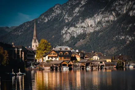 HD PC desktop wallpaper of Hallstatt, Austria — quaint lakeside town with a tall church steeple reflected on the calm lake beneath steep Alpine cliffs.