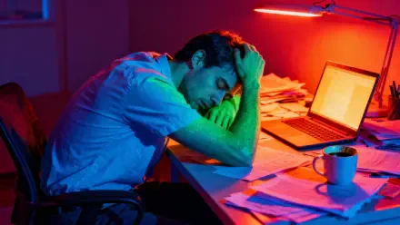 Burnt out — 4K Ultra HD PC desktop wallpaper of an exhausted person slumped over a cluttered desk in red-blue neon light, with a laptop, scattered papers and a coffee mug.