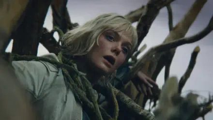 HD PC desktop wallpaper: the lead actress from the movie Predator: Badlands — pale-haired woman tangled in gnarled roots, gazing upward amid moody, dramatic lighting.