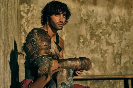 HD PC desktop wallpaper/background from the TV show Spartacus: House of Ashur — a leather-armored warrior with dark curls leaning against a weathered stone wall.