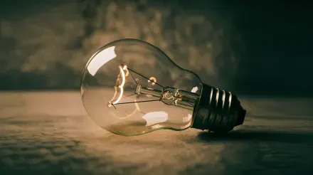 Vintage incandescent light bulb with warm glowing filament on a textured surface, 4K Ultra HD PC desktop wallpaper and background.