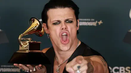 2K Quad HD desktop wallpaper of a punk-rock singer at the Grammy Awards, heavy eye makeup, clutching a Grammy trophy and pointing aggressively toward the camera, music energy and stage presence.