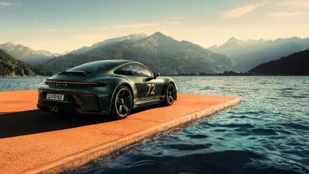 Green Porsche 911 GT3 parked on an orange lakeside pier with soaring mountains at sunrise — 4K Ultra HD PC desktop wallpaper/background.