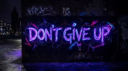 Neon DON'T GIVE UP graffiti in purple and blue glowing on a wet, dark brick wall with pavement reflections — 5K Ultra HD PC desktop wallpaper/background.