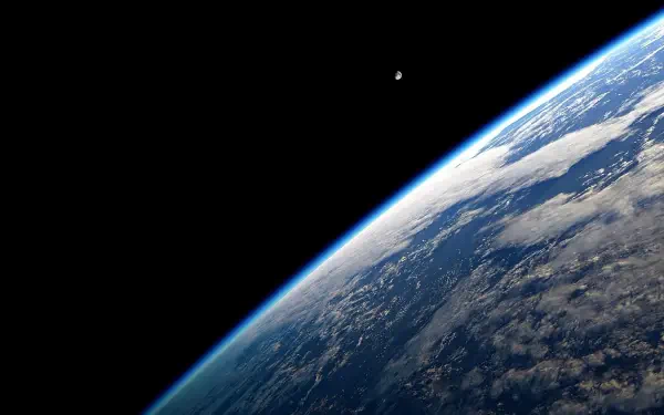 HD PC desktop wallpaper: space view of a planet from orbit—curved, cloud-covered surface with a bright limb and a small distant moon.